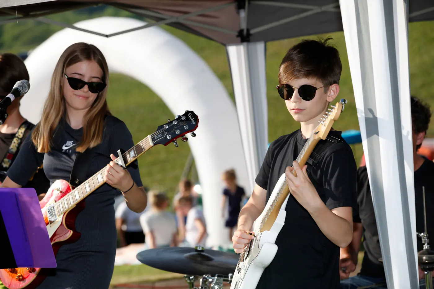 Eine Sängerin mit E-Gitarre und ein Gitarrist, beide mit Sonnenbrille, spielen in einer Schülerband im Freien