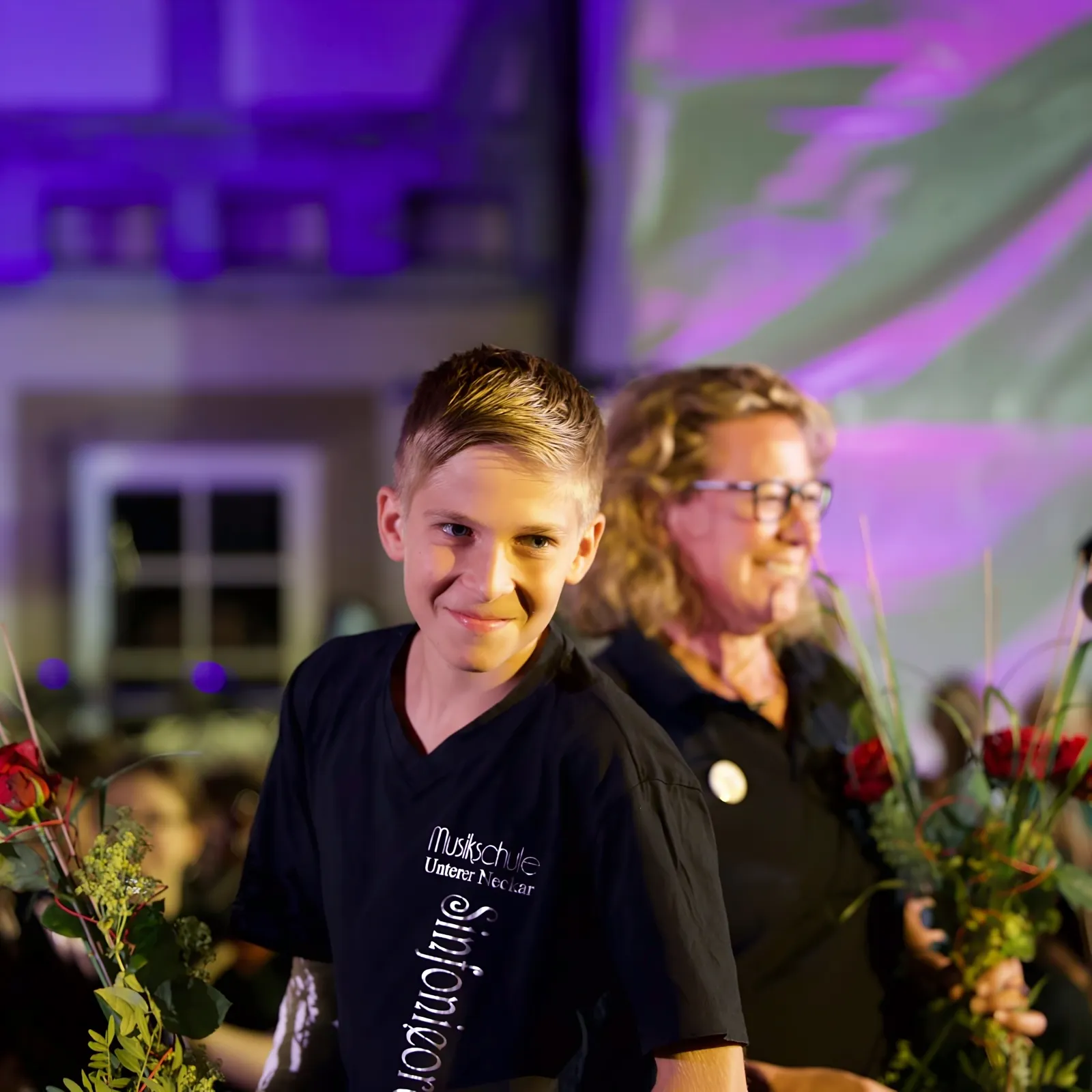 Ein Junge aus dem Sinfonieorchester strahlt nach dem Konzert, neben ihm Blumensträuße
